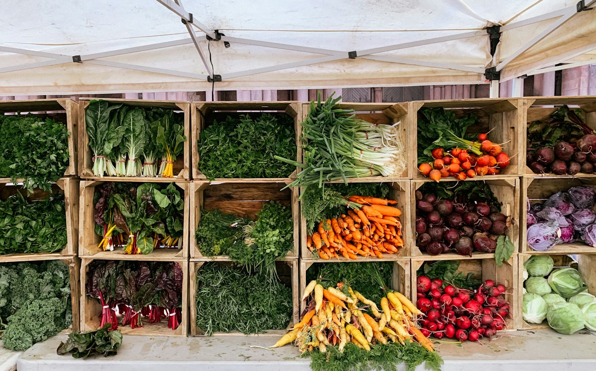 Fresh carrots, beets, radishes, cabbages and leafy greens arranged in wooden crates at an outdoor farmers market